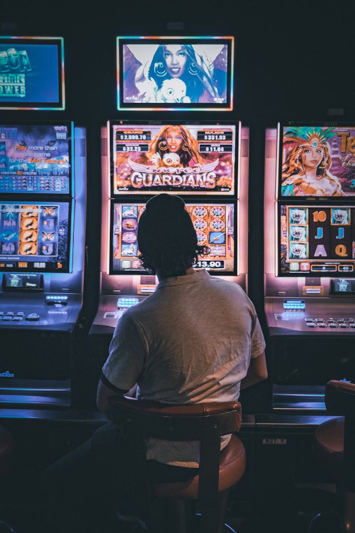 ours-journey Adult male seated in a dimly lit casino engaging with vibrant slot machines at night.